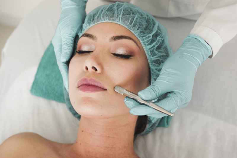 Profesional con guantes y gorro realizando un tratamiento facial a una clienta en cabina