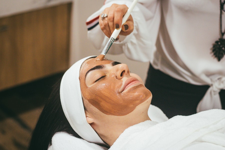 Esteticista aplicando con pincel una mascarilla facial a una clienta tumbada en la camilla